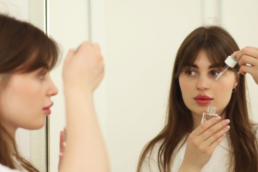 A young woman applying skincare serum in front of a mirror