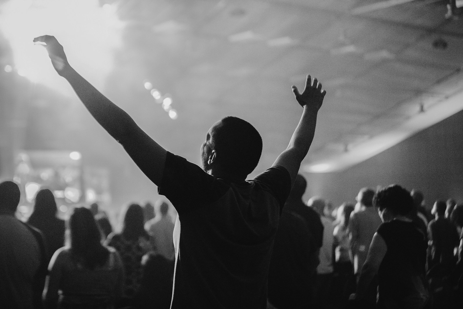Worshipper with arms raised toward a bright stage light during I Speak Jesus
