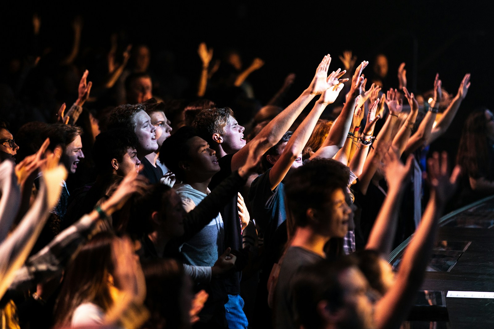 People raising their hands at a night worship gathering declaring the mighty name of Jesus